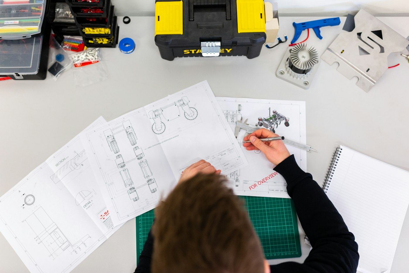 Tecnico al tavolo che disegna schemi su fogli di progetto, con attrezzi e strumenti di misura